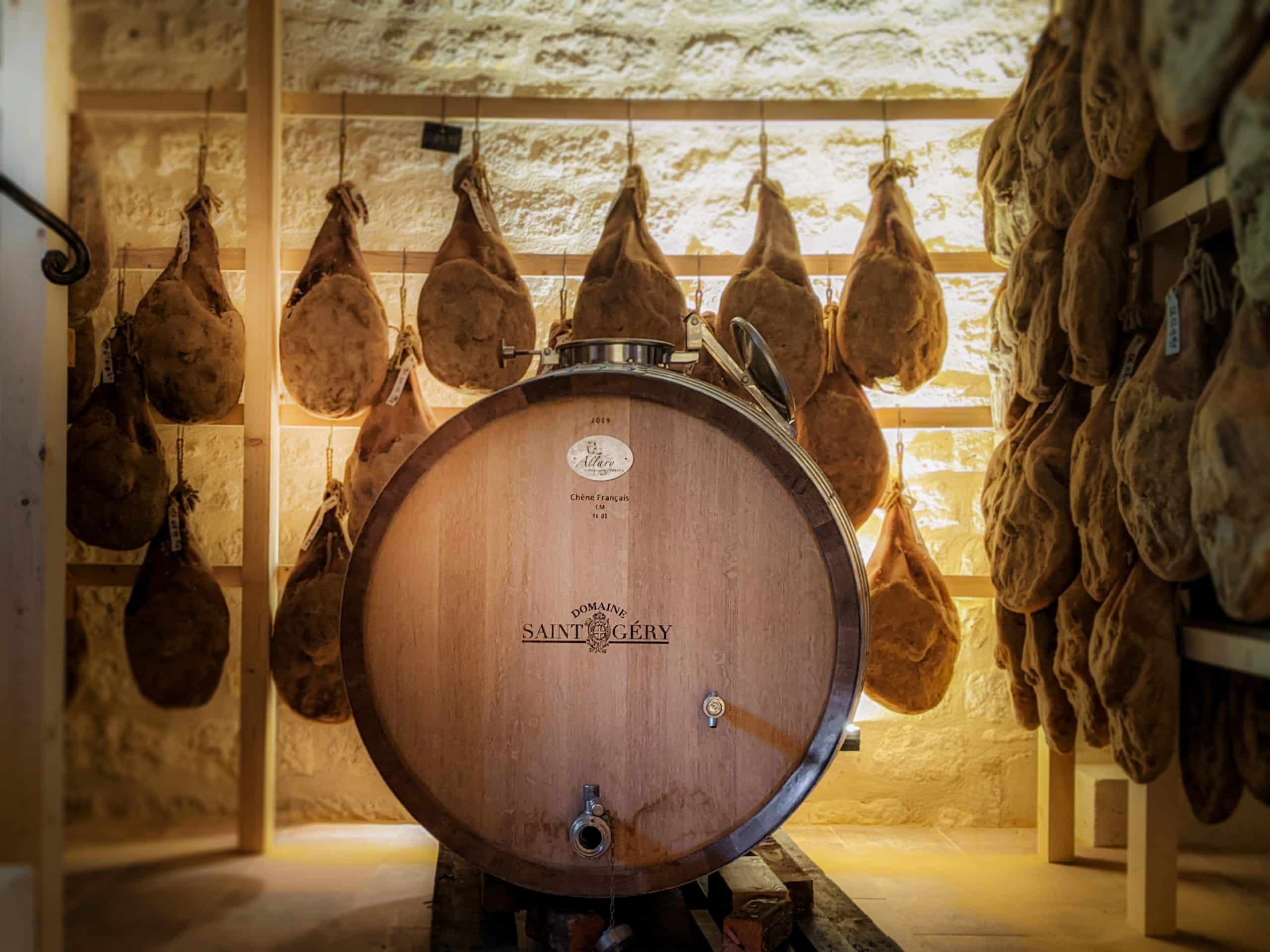 Barrique de vin au milieu de la cave d'affinage où pendent les jambons Patrick Duler